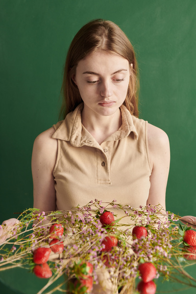 A woman with long brown hair looking at pink wildflowers and strawberries laid out on a round mirror