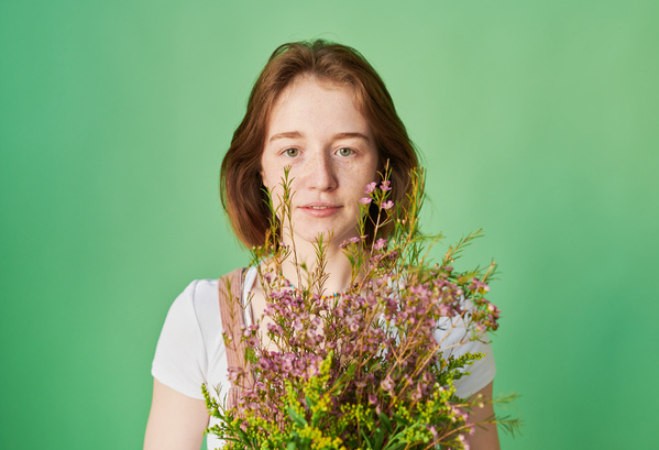 A young woman with short red hair with a bouquet of pink and yellow wildflowers against a green background