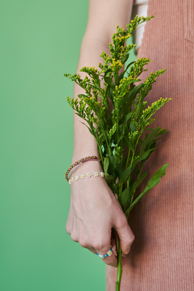 A sprig of yellow wildflowers in the hand of a woman with beaded jewelry dressed in a corduroy sundress