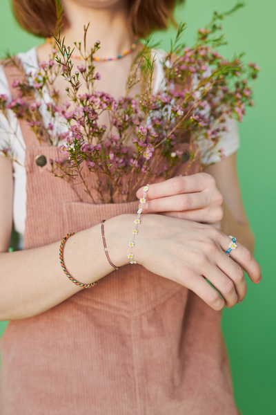 A woman with beaded jewelry bracelets and pink wildflowers decorating the pocket of a pink corduroy sundress