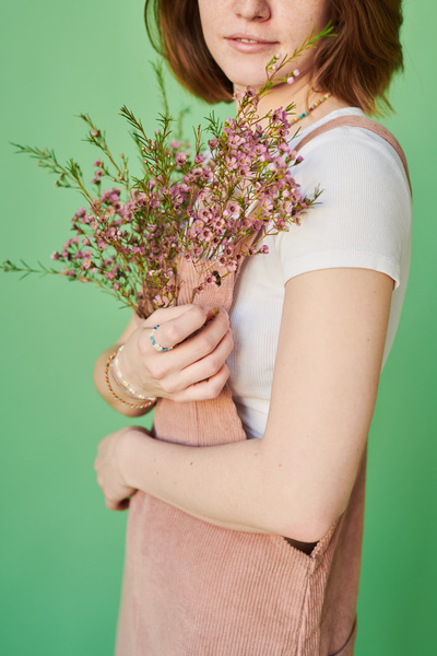 A woman with beaded jewelry bracelets has pink wildflowers adorning the pocket of a pink corduroy sundress