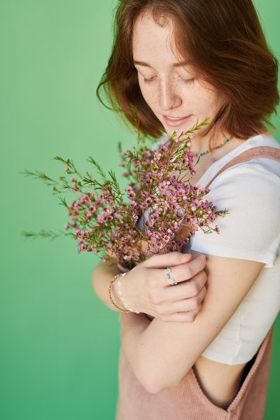 A woman with ginger hair dressed in a pink corduroy sundress adorned with pink wildflowers posing against a green background