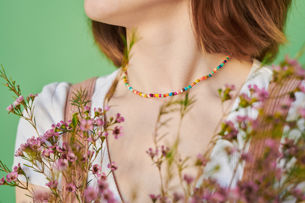 Pink wildflowers adorning a corduroy summer sundress of a red-haired woman with a bright beaded necklace