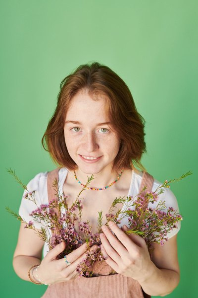A beautiful red-haired woman dressed in an outfit decorated with pink wildflowers poses against a green background