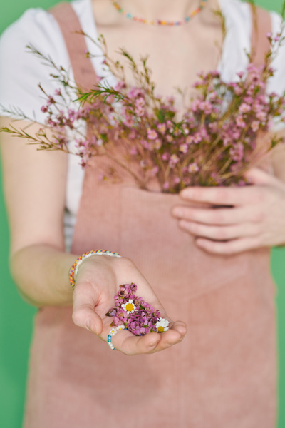 A woman in a summer corduroy sundress adorned with flowers holding buds of pink wildflowers in the hand