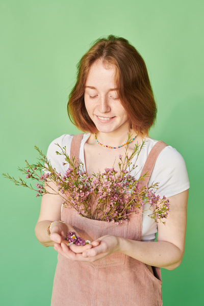 A young woman with red hair in a pink corduroy sundress with pale pink wildflowers in her pocket and flower buds in her hand