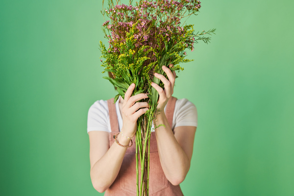 A woman hiding behind a bunch of pink and yellow wildflowers against a green background