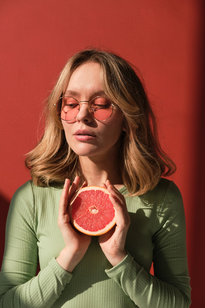 A woman with fair hair in a mint-colored longsleeve and sunglasses posing with half a grapefruit