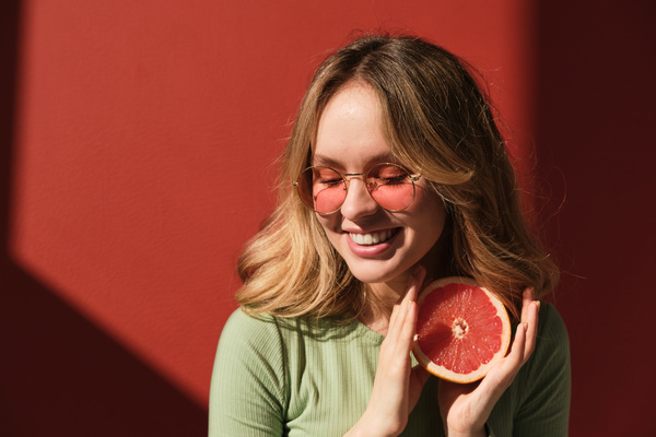 A woman in a mint-colored longsleeve and sunglasses looking down with a half a grapefruit in her hands