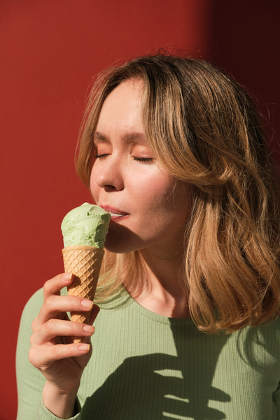 A woman with short blonde hair dressed in a green blouse eating pistachio ice cream in a cone
