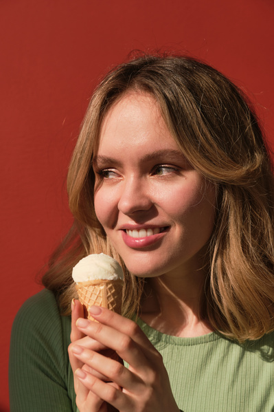 A smiling woman with short blonde hair wearing a green blouse with vanilla ice cream in a cone against a red background