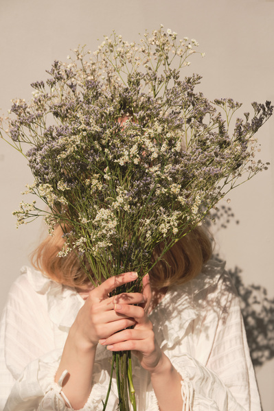 A woman with blonde hair dressed in white hiding her face with a bouquet of light wildflowers
