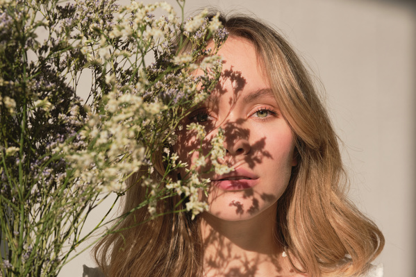 A woman with blond hair looking out behind a bouquet of wildflowers in a sunny room