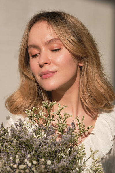 Portrait of a blonde woman with blonde hair looking at a bouquet of small wildflowers near her face in a sunny room