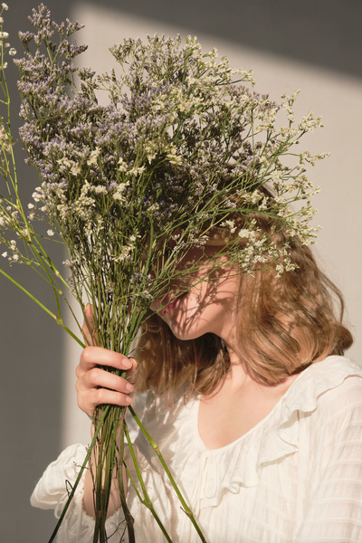 A blonde haired woman hiding her face behind a bouquet of small flowers in a sunny room