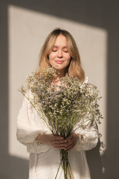 A blonde haired woman in a white summer dress holding a bouquet of wildflowers standing against a white background