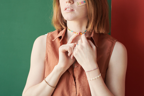 A red-haired woman in a red sleeveless blouse twirling a multicolored beaded necklace on her finger