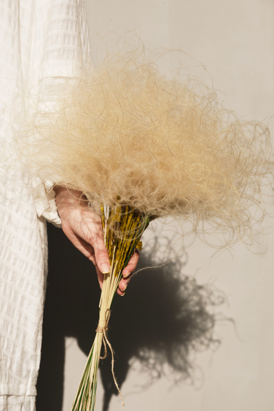 Bouquet of golden field dried flowers in the hand of a woman in a white dress