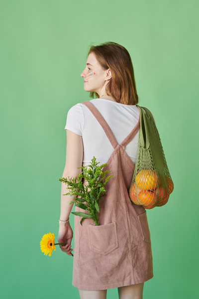A woman with red hair in a summer outfit with flowers and citrus fruits in a green cotton string bag standing back