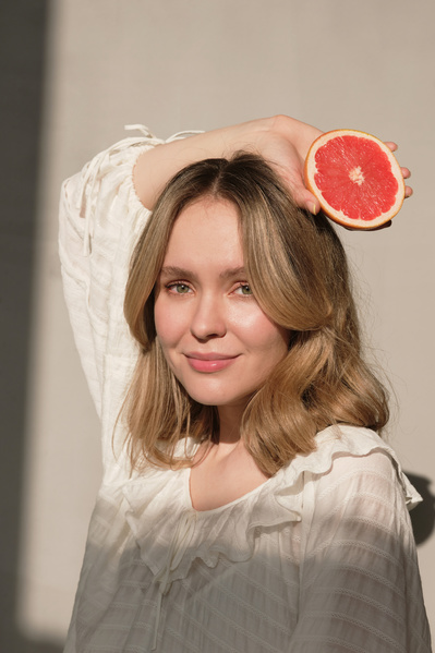 A woman in a white dress poses with half a grapefruit in her hand