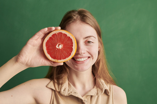 A woman with brown hair dressed in a beige polo shirt hiding her eye with half a grapefruit