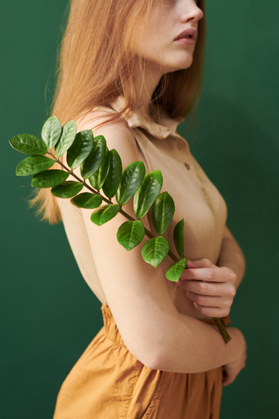 A woman with long brown hair dressed in an outfit of warm shades holding a twig with green leaves