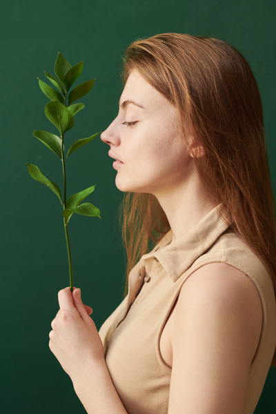 Profile of a woman with brown hair dressed in a beige T-shirt with a twig with green leaves in front of her face