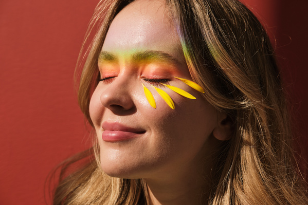 Yellow gerbera petals and rainbow rays on the face of a smiling woman with blonde hair and closed eyes