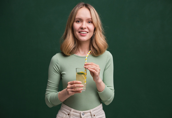 Beautiful woman with flowing light hair in a dress of light shades with lemonade in a glass with a straw