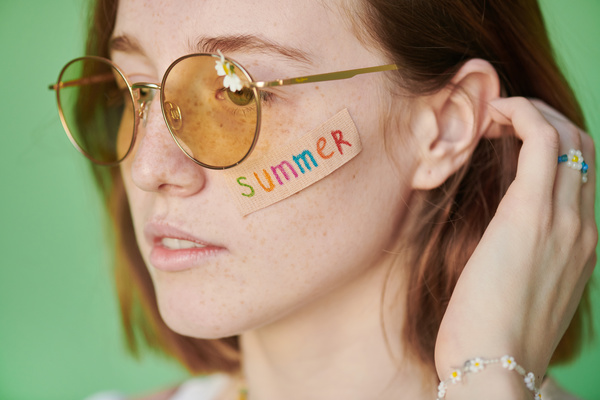 Summer sticker on the face of a woman in yellow sunglasses with a daisy straightening red hair