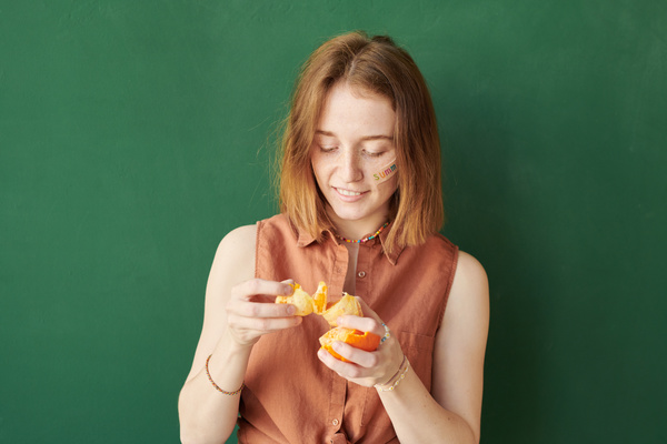 A woman with short red hair and a summer sticker on her face dividing peeled tangerine into segments