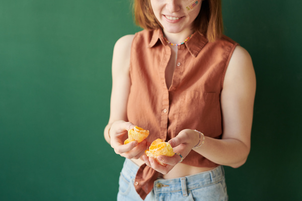 Close-up of a peeled and divided into segments tangerine in the hands of a smiling woman with a red bob