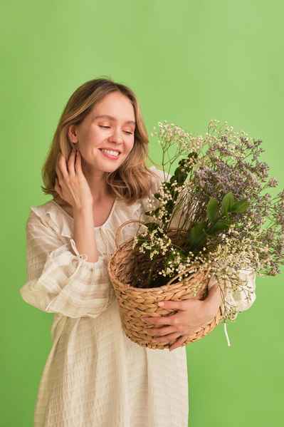 A smiling woman with blonde hair dressed in a white summer clothes with a braided basket of wildflowers