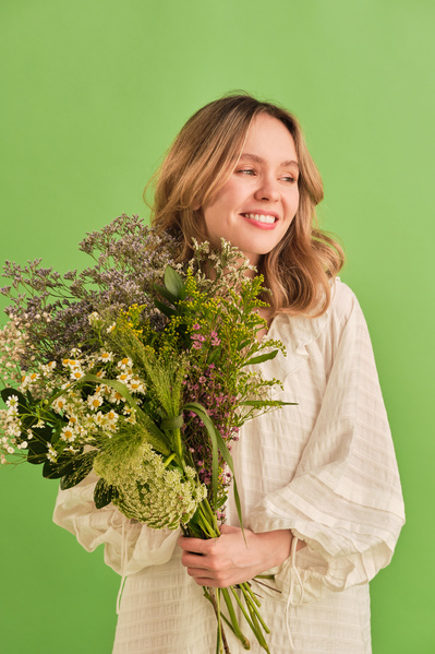 A woman with blonde hair dressed in a white light dress with bouquet of multicolored wildflowers