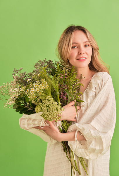 A woman with blonde hair dressed in a white summer dress embracing bouquet of colorful wildflowers
