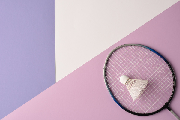 Badminton racket with a white shuttlecock lying on the surface ot the pastel shades