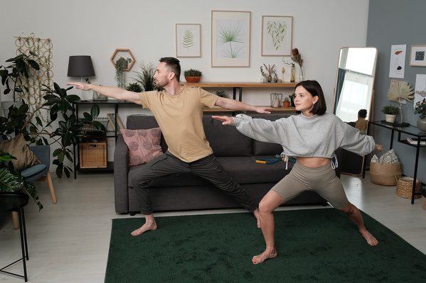 A young woman in a sports outfit and a man in loose clothes practicing yoga asanas in a living room