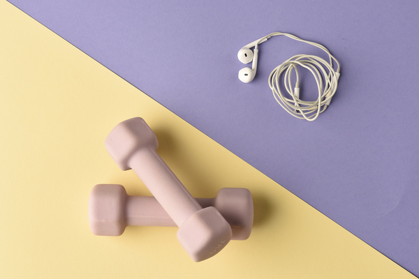 Pink fitness dumbbels on a yellow surface and white wired headphones on a purple surface