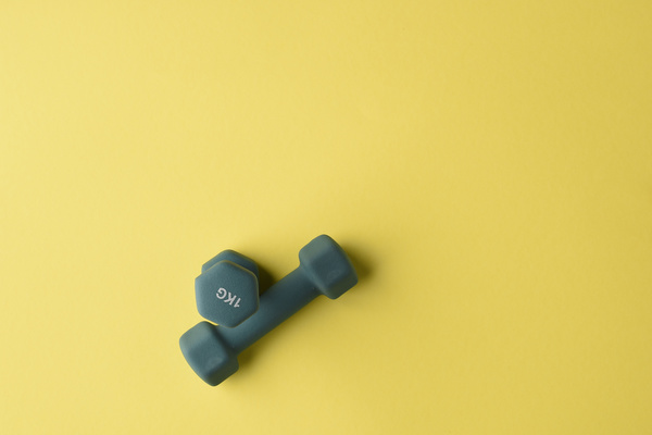Top view of green fitness dumbbells lying on a yellow surface