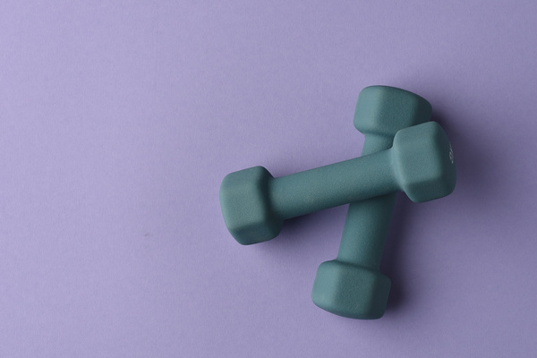 Gray fitness dumbbels lying on each other on a purple surface