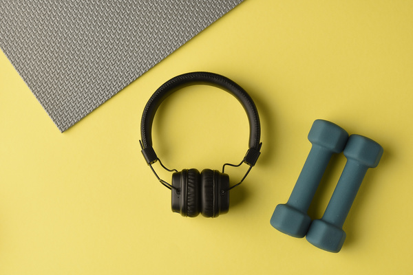 Top view of black headphones and dark dummbels lying on a bright yellow surface