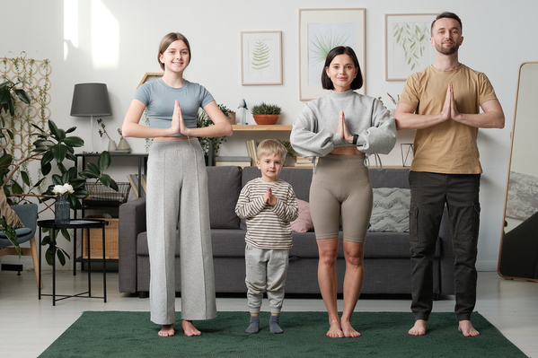A a family of four members children wearing home clothes practicing yoga on the carpet in a livingroom