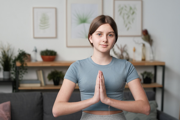 A teenage girl with tidied up hair in a grey T-shirt doing namaste at home