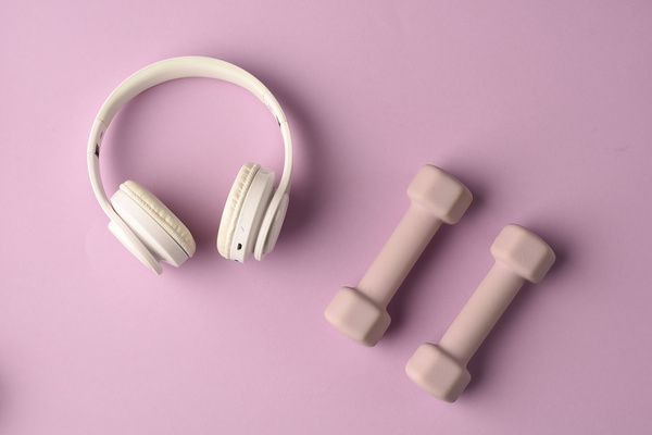 White headphones and pink weights for fitness lying on a pastel-colored surface