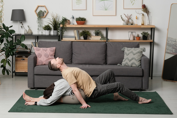 A man in a yellow T-shirt and his dark-haired wife practicing yoga at home