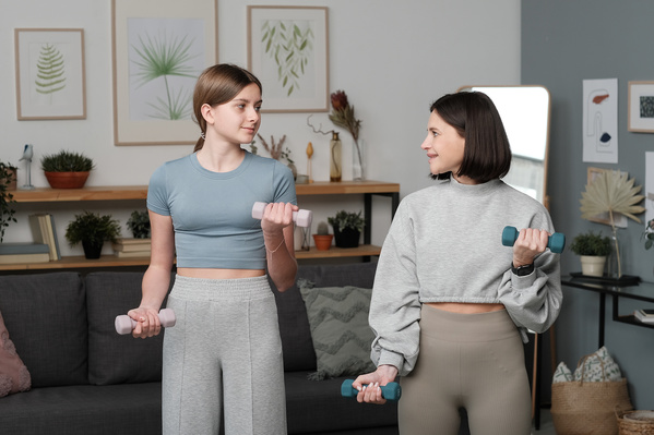 A teenage girl in light sports clothes and her mom with short dark hair doing an exercise with weights