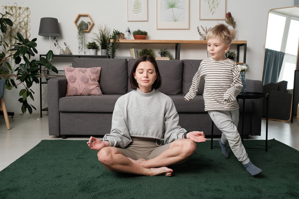 A woman with dark hair dressed in gray sportswear meditates while her son having fun