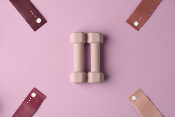 Dumbbells of a delicate shade surrounded by elastic bands for sports on a pink background