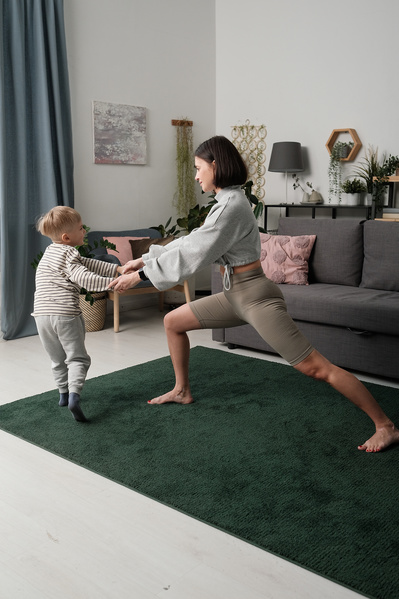 A woman with short dark hair performing a lunge and her son holding her hands