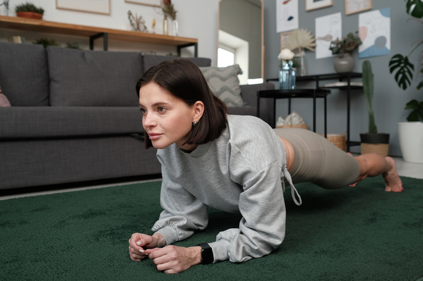 A beautiful woman with short dark hair performing a plank on a green carpet in a living room